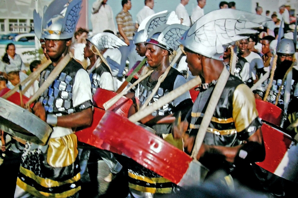 Carnival musicians in helmets playing drums in a street parade in Aruba, 1961