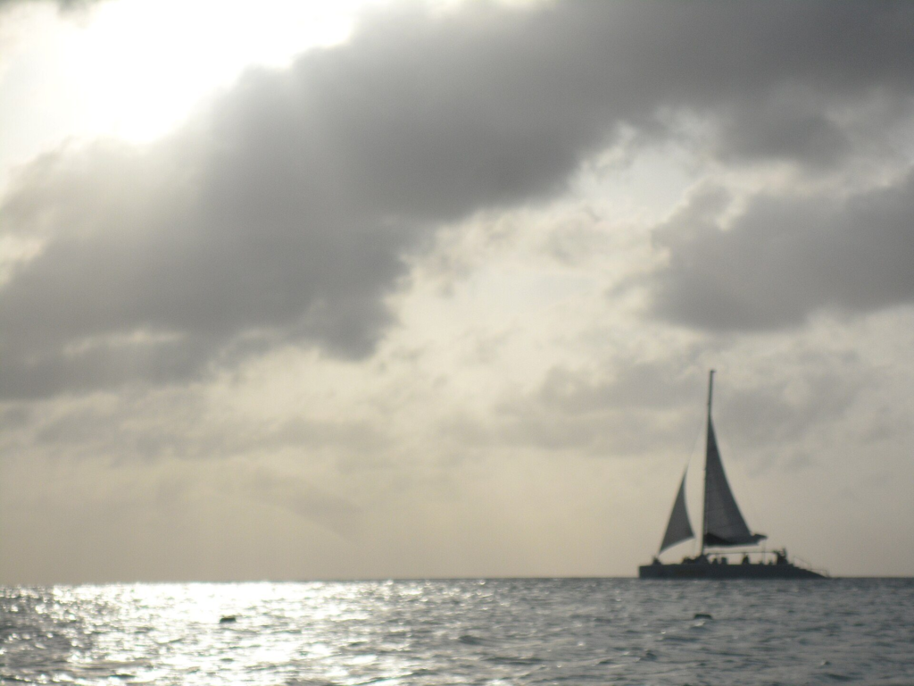 A catamaran sailing off Eagle Beach, Aruba, under a cloudy evening sky
