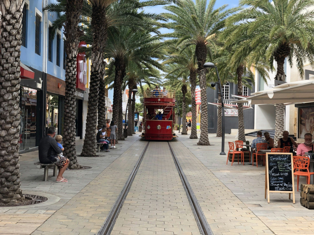 Red trolley car on a palm-lined street near the Oranjestad cruise port