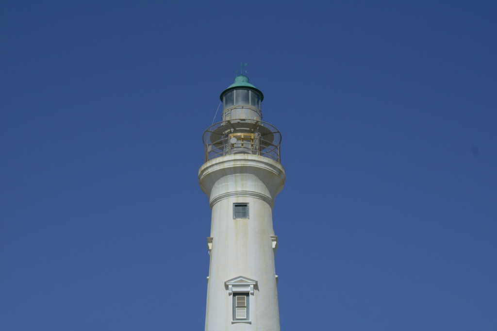 A white lighthouse with a green top against a blue sky in Aruba