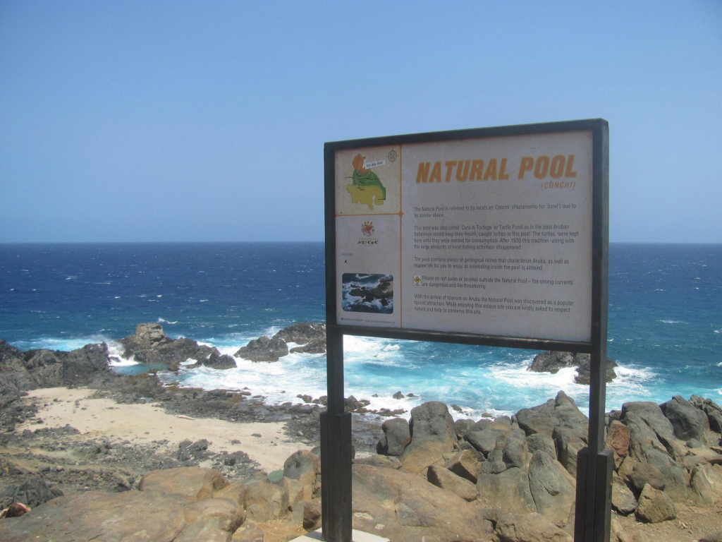 The Natural Pool information sign above the rocky coast in Arikok National Park