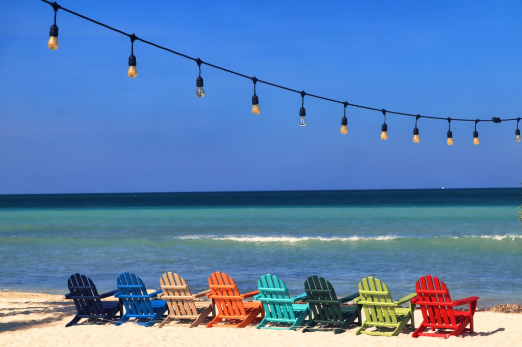 Colorful chairs facing the sea under hanging lights on a beach in Oranjestad, Aruba