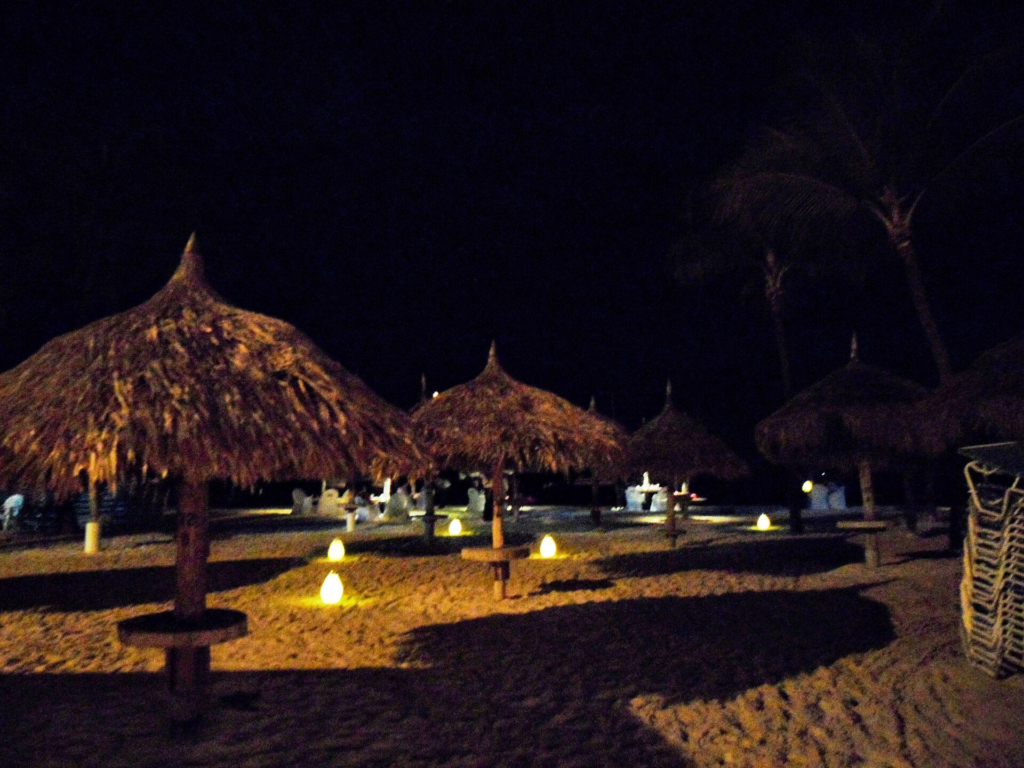 Lit palapa umbrellas on Eagle Beach at night
