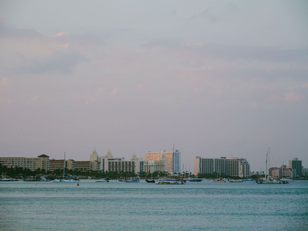 Coastal Oranjestad at twilight, with boats on the water and buildings along the shore