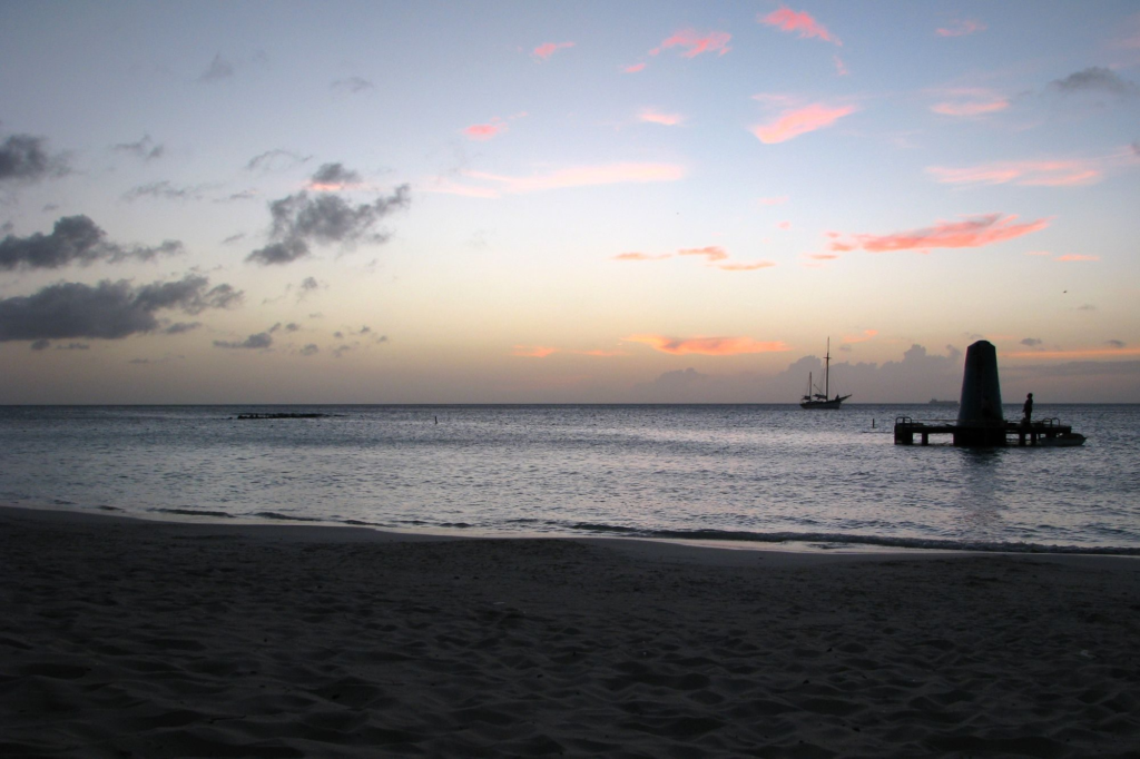 A pier and boat silhouetted against a purple twilight sky over a calm Aruba beach
