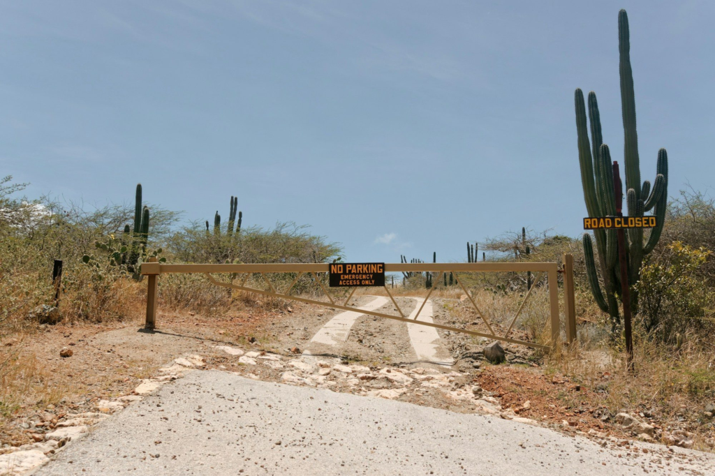 Dirt trail leading past cacti and a gate in Arikok National Park, Aruba