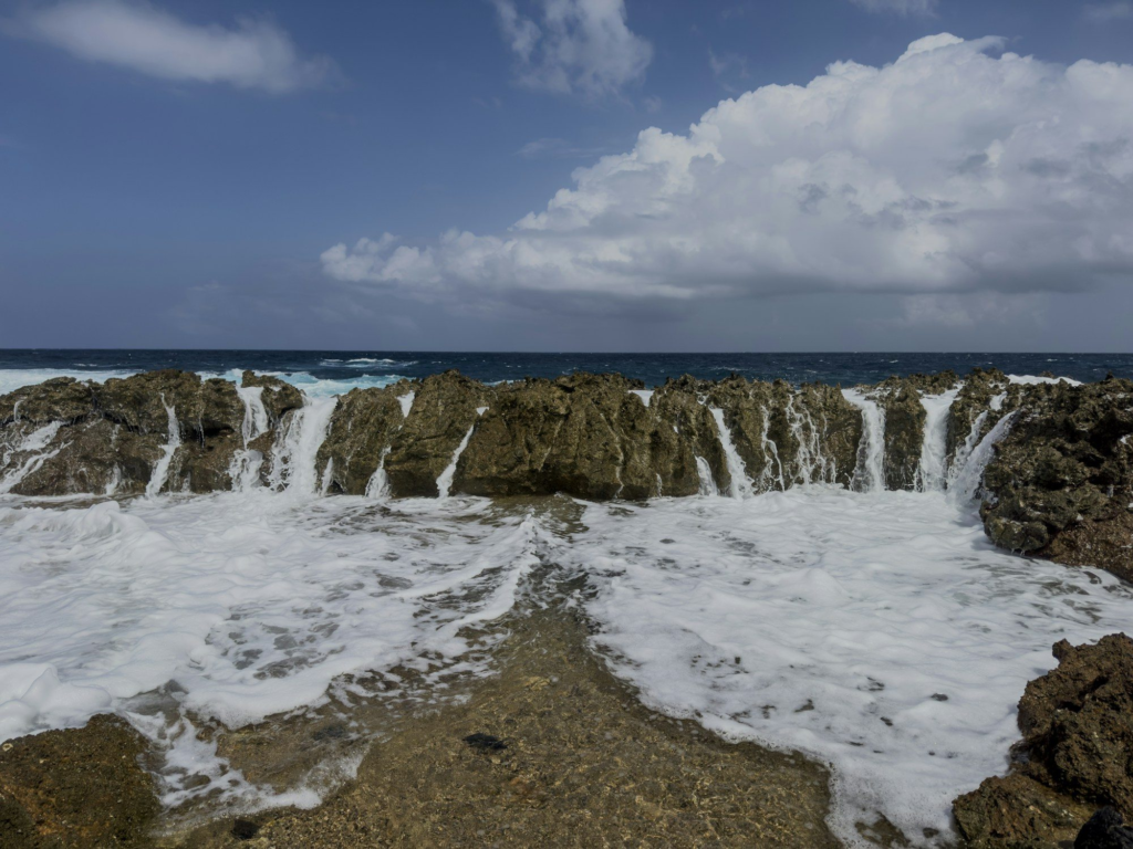 Waves crashing against Aruba's rocky north shore under a cloudy sky